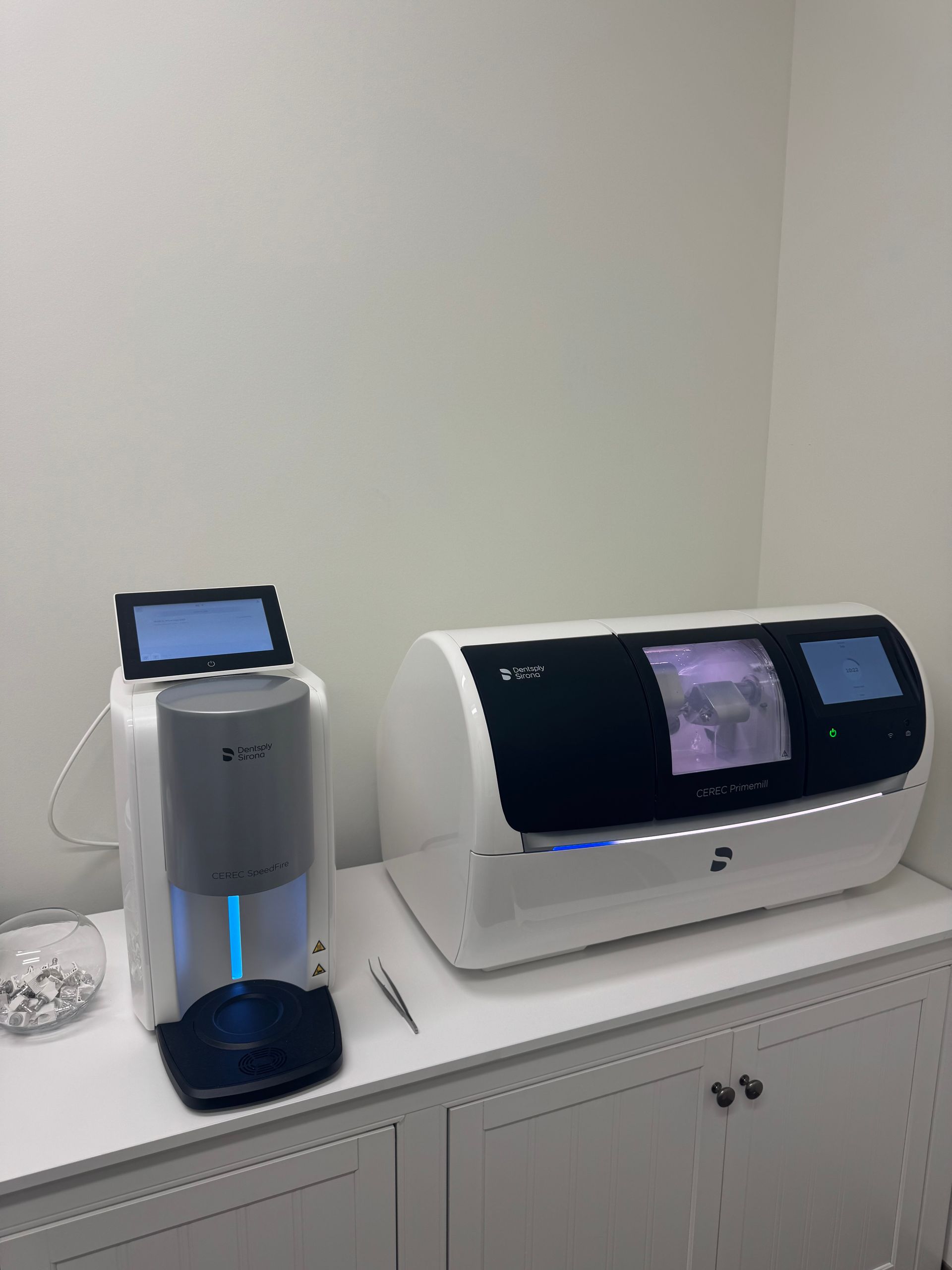 Dental office equipment: milling machine and scanner on a white cabinet.