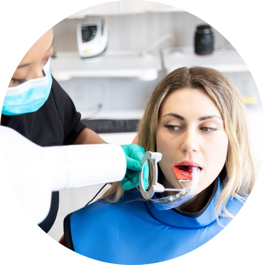Dentist taking dental X-ray of a patient. Patient in blue protective vest. Doctor wears mask, green gloves.