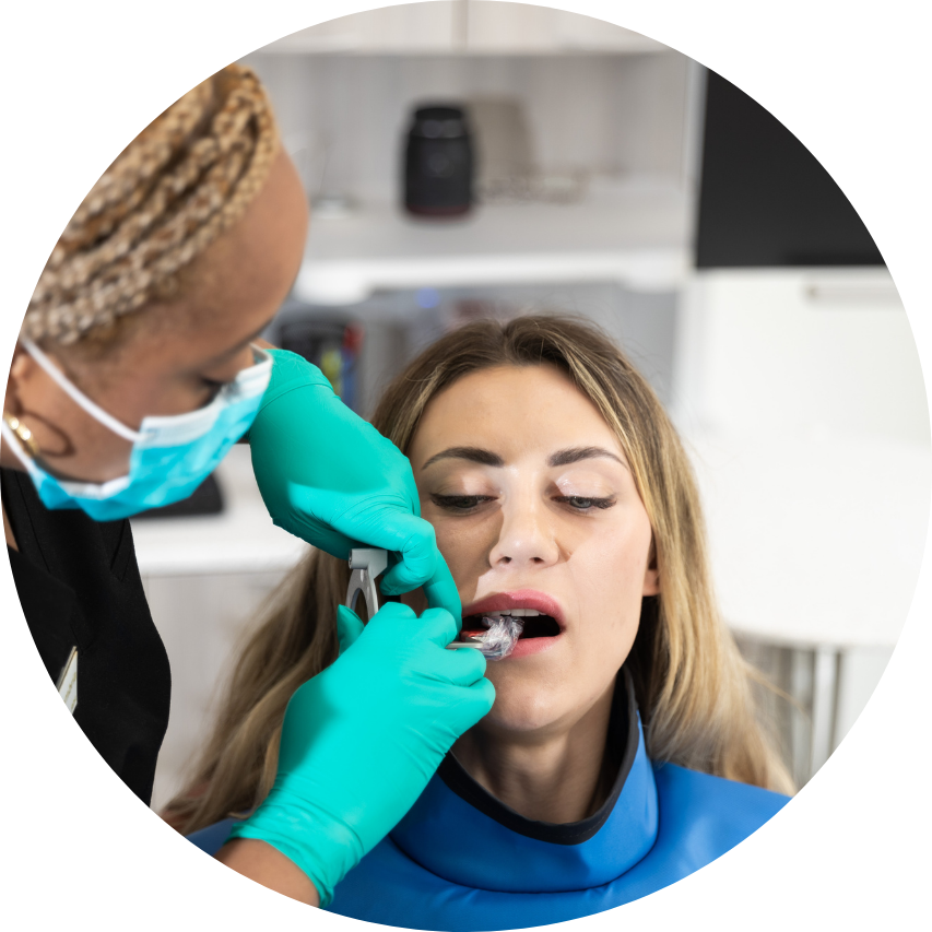 Dentist taking x-ray of patient's teeth. Dentist wears mask, gloves. Patient's mouth held open with instrument. Blue bib.