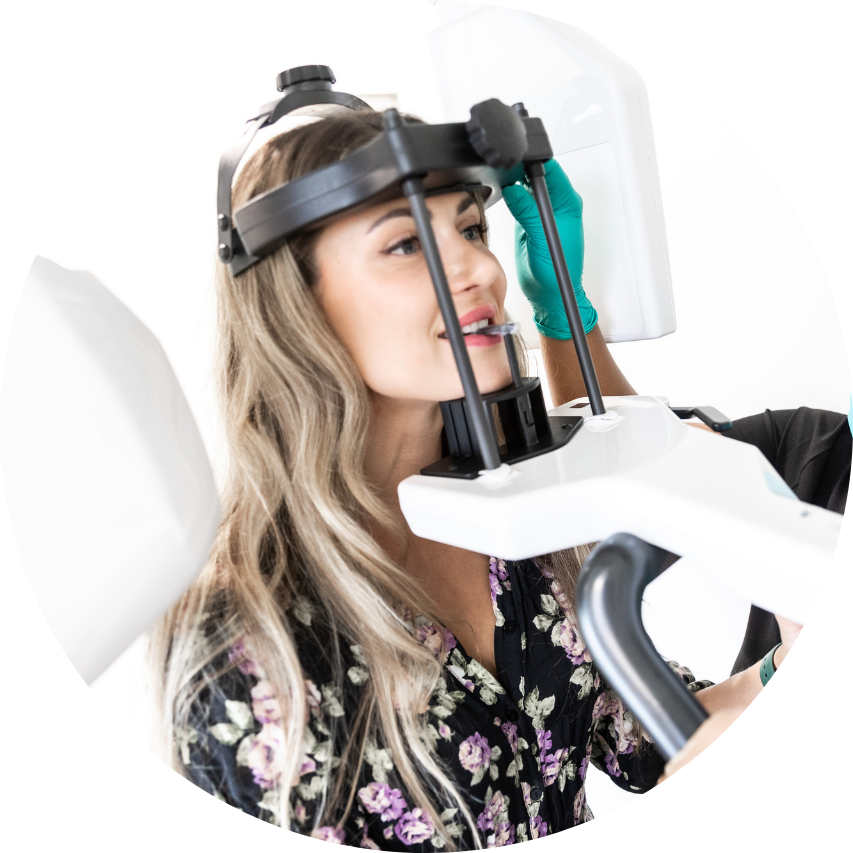 Woman wearing dental X-ray machine with a professional wearing green gloves adjusting it.