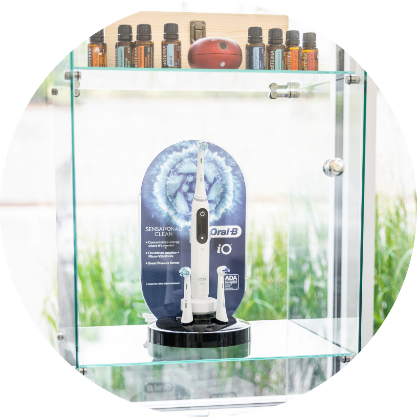 Electric toothbrush in a glass display case with essential oil bottles on a shelf above.
