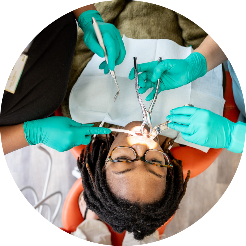 Person in dentist chair, mouth open, receiving dental work. Gloved hands holding tools.
