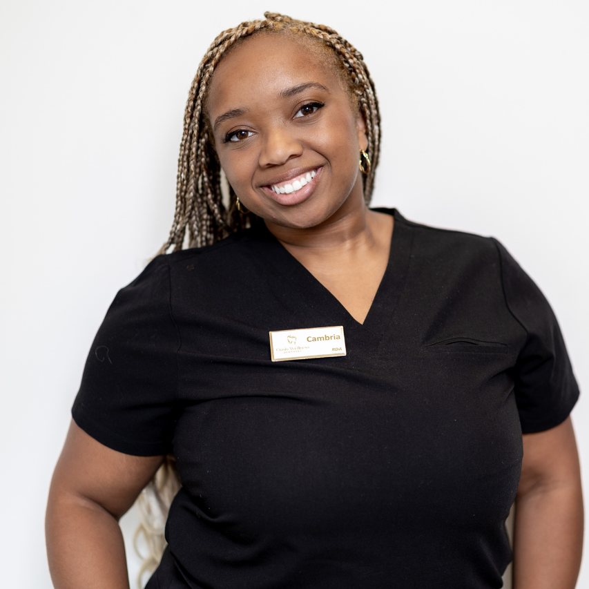 Woman with blonde braids wearing black scrubs smiles at the camera.