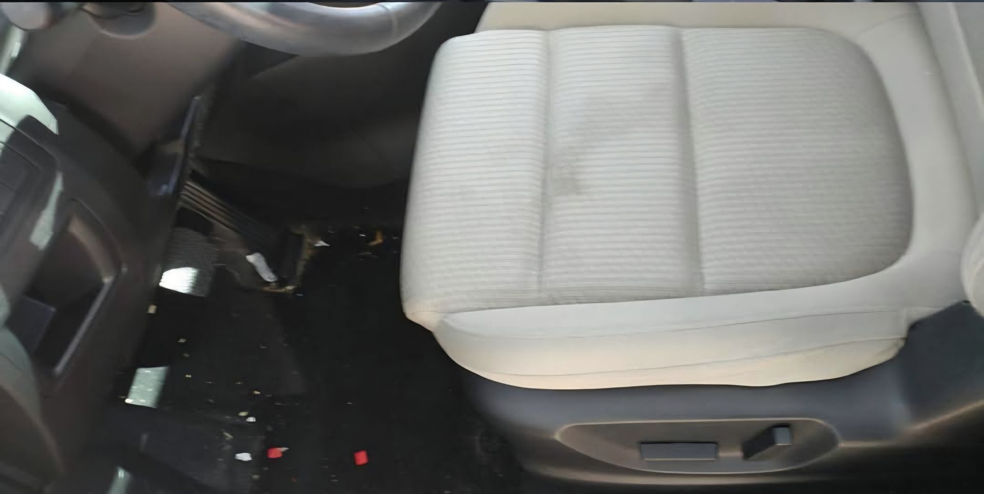 Car interior with a light-colored fabric seat, showing a dark stain. The steering wheel is visible.