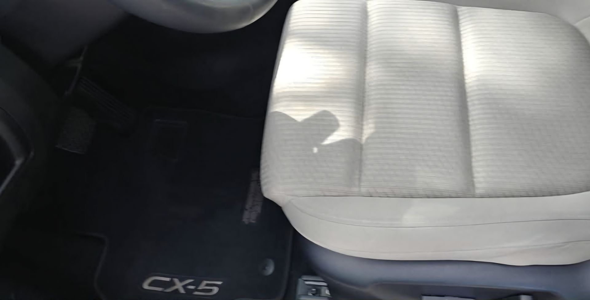 Interior car view, showing a light-colored seat, black floor mat with