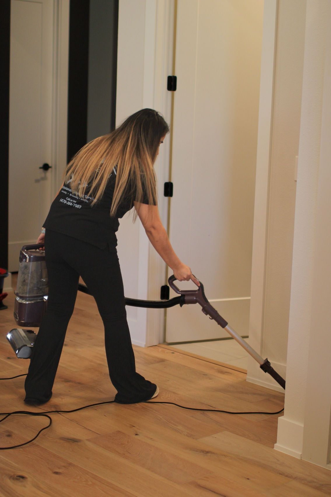 Person vacuuming a wooden floor in a hallway with white walls and a doorway. Person vacuuming a wooden floor in a hallway with white walls and a doorway.