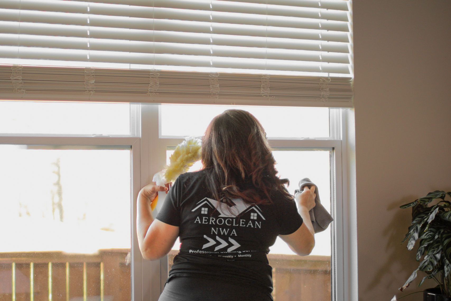 Woman cleaning a window, holding cloths, with a company logo shirt. Woman cleaning a window, holding cloths, with a company logo shirt.