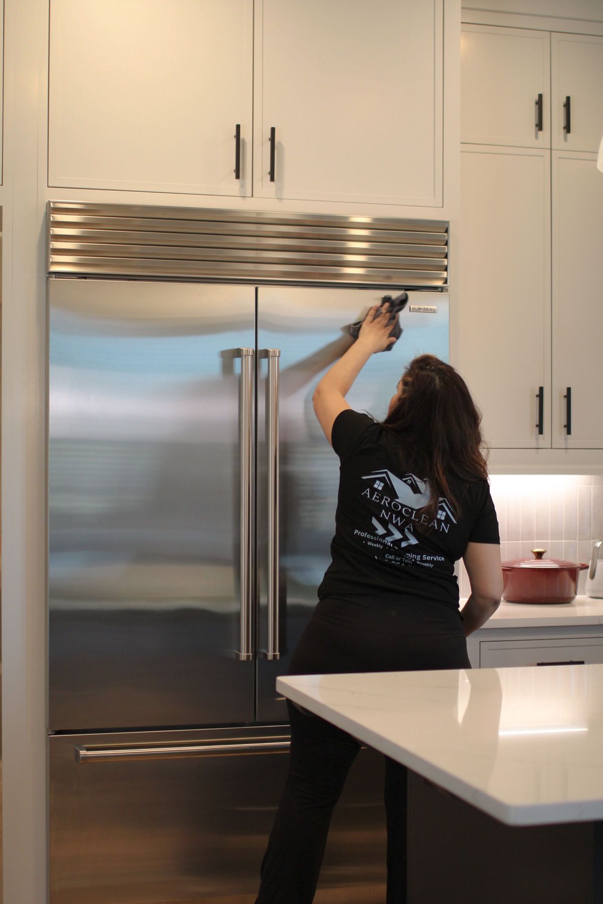 Person standing in a kitchen reaches toward the top of a large refrigerator. Person standing in a kitchen reaches toward the top of a large refrigerator.