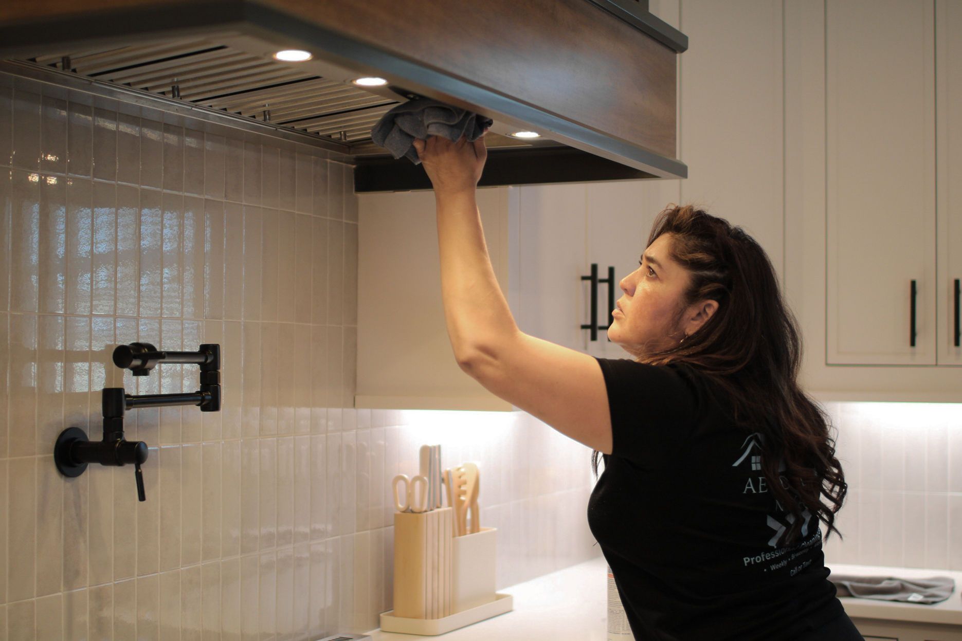 Woman cleaning kitchen range hood with a cloth.