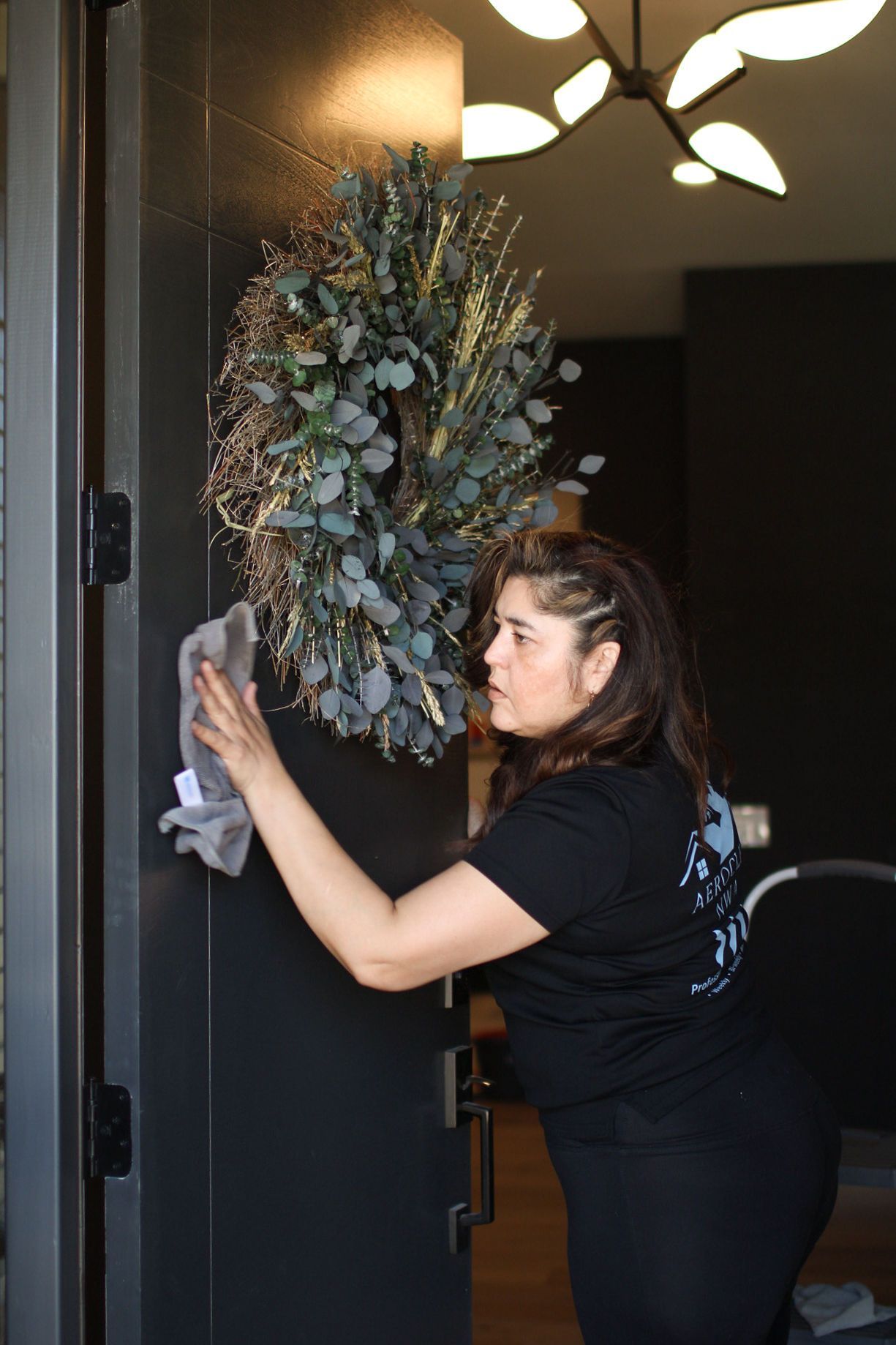 Woman wiping front door with a cloth, wreath on door. Woman wiping front door with a cloth, wreath on door.