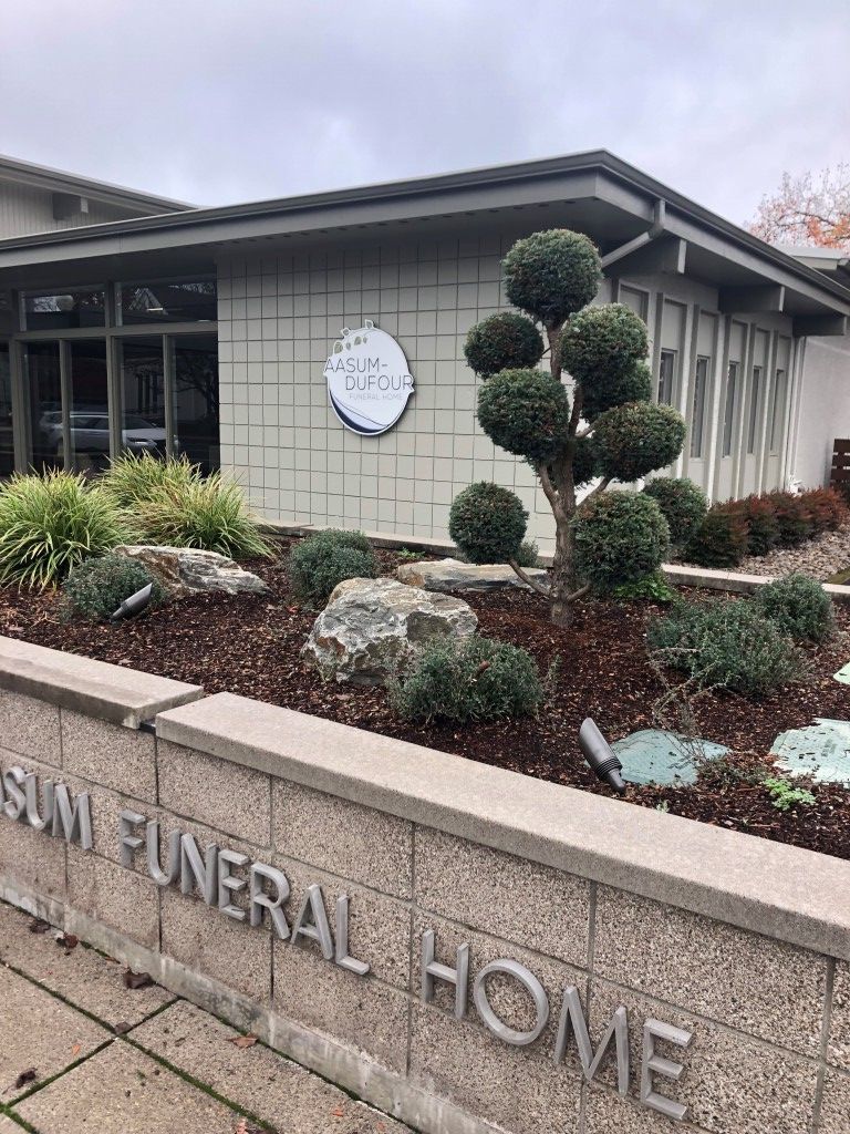 Exterior of a funeral home with landscaping. Sign on wall,