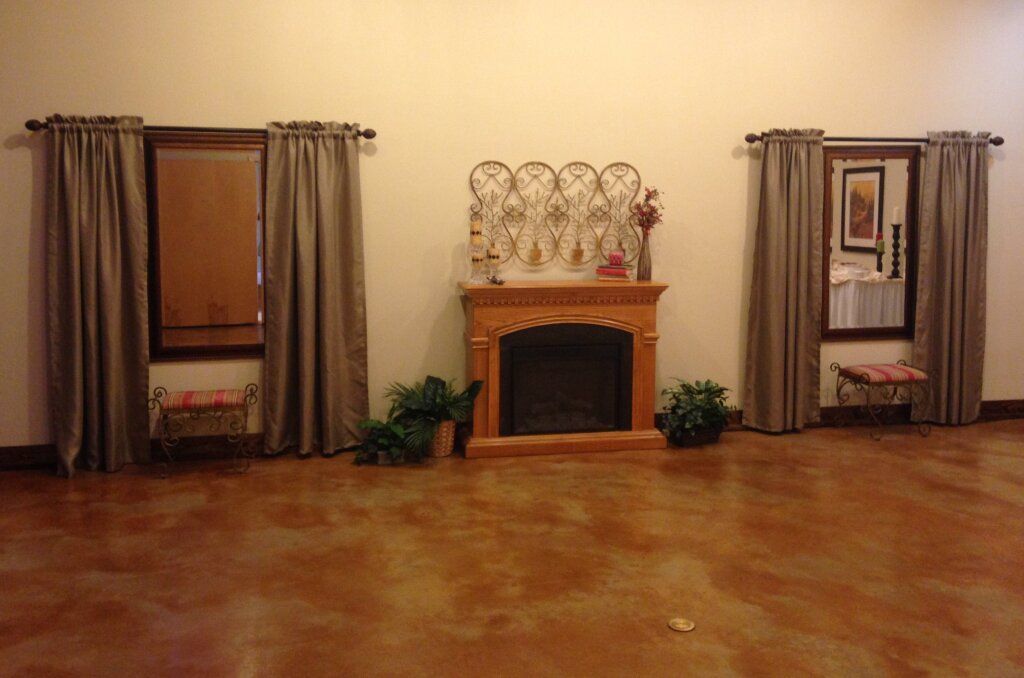 A room with a fireplace centered between two windows with curtains, and a brown floor.