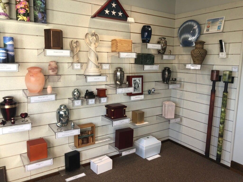 Display of cremation urns on shelves in a room, including various shapes, sizes, and colors.