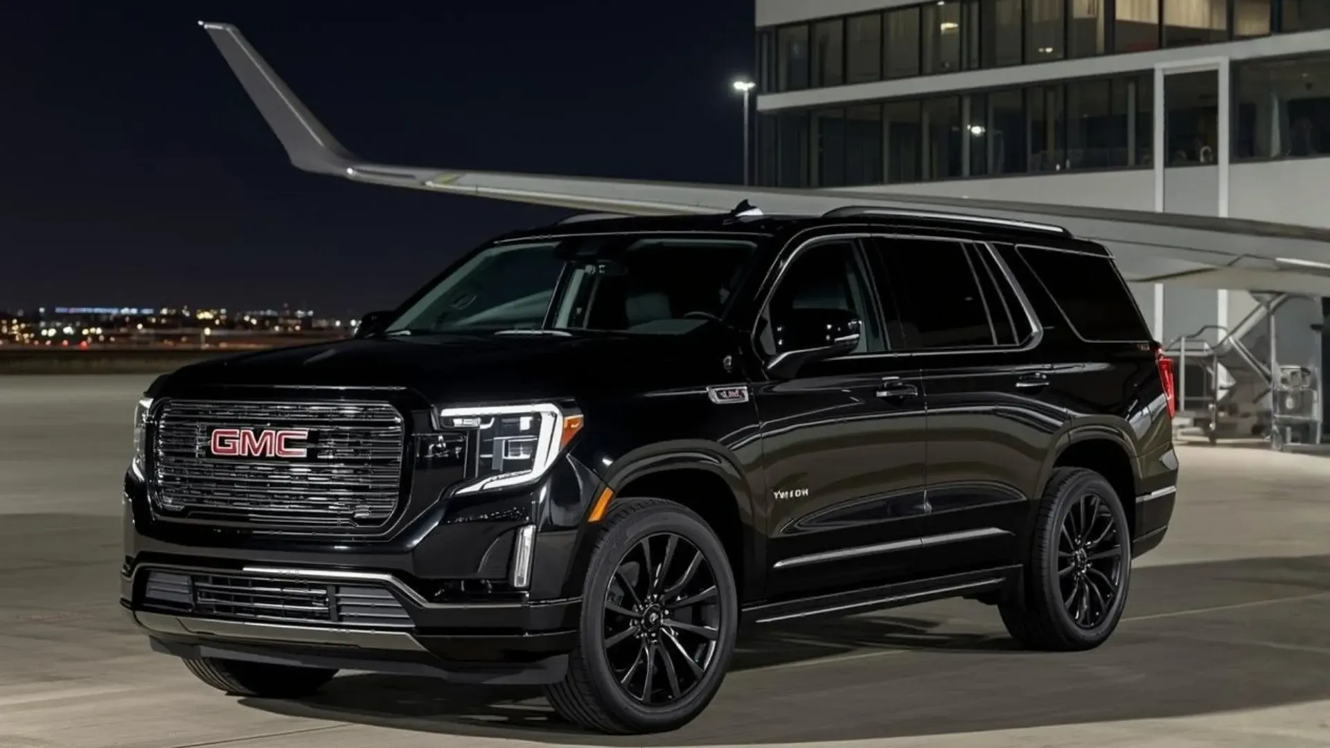 Black GMC Yukon SUV parked near an airplane, at night.