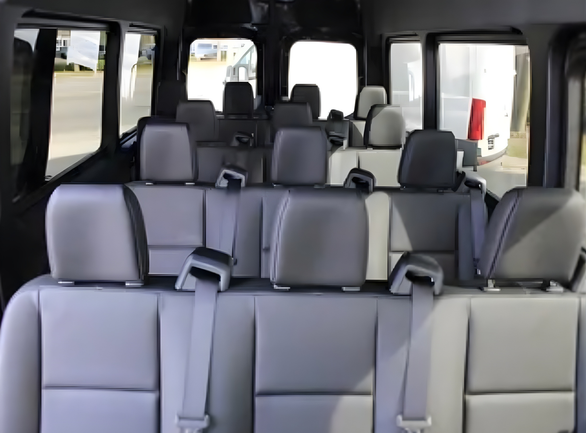 Interior view of a passenger van with rows of gray seating and headrests; empty.