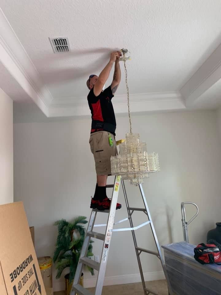 A man is standing on a ladder fixing a chandelier.