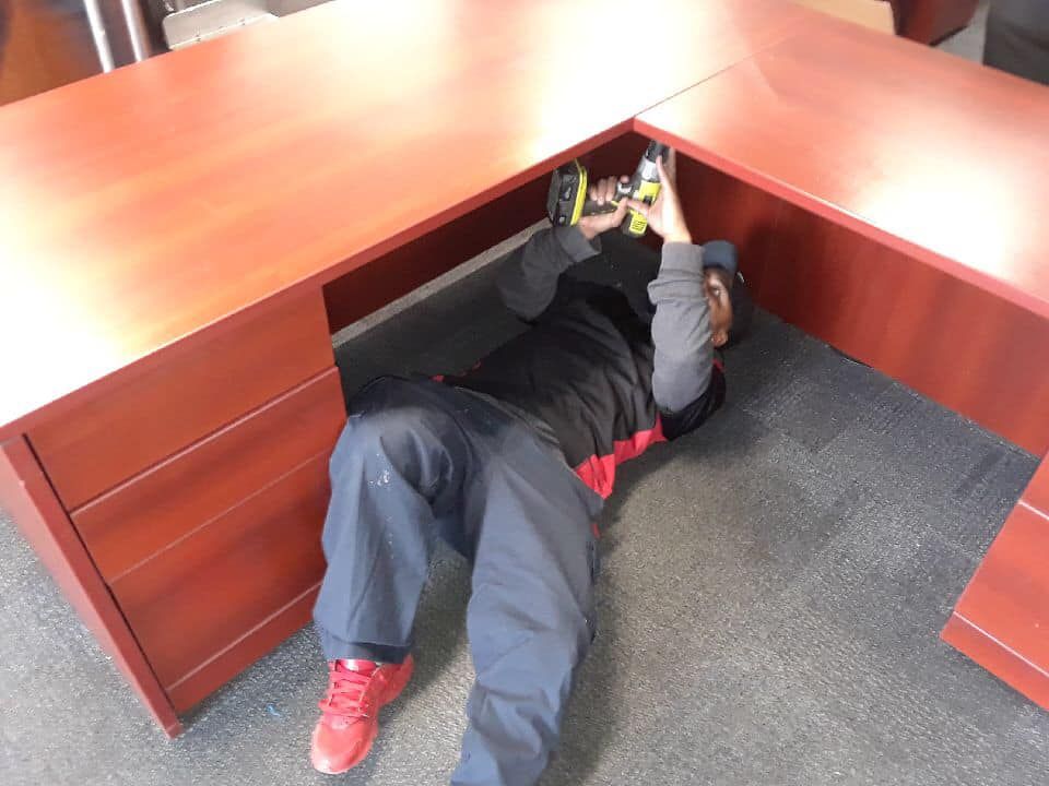 A man is laying under a desk using a tape measure 28.4845° N, 81.2519° W
