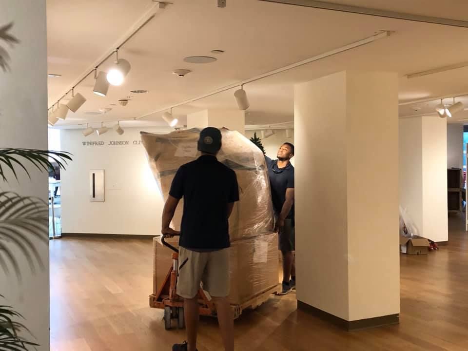 Two men are moving a large box on a dolly in a room.