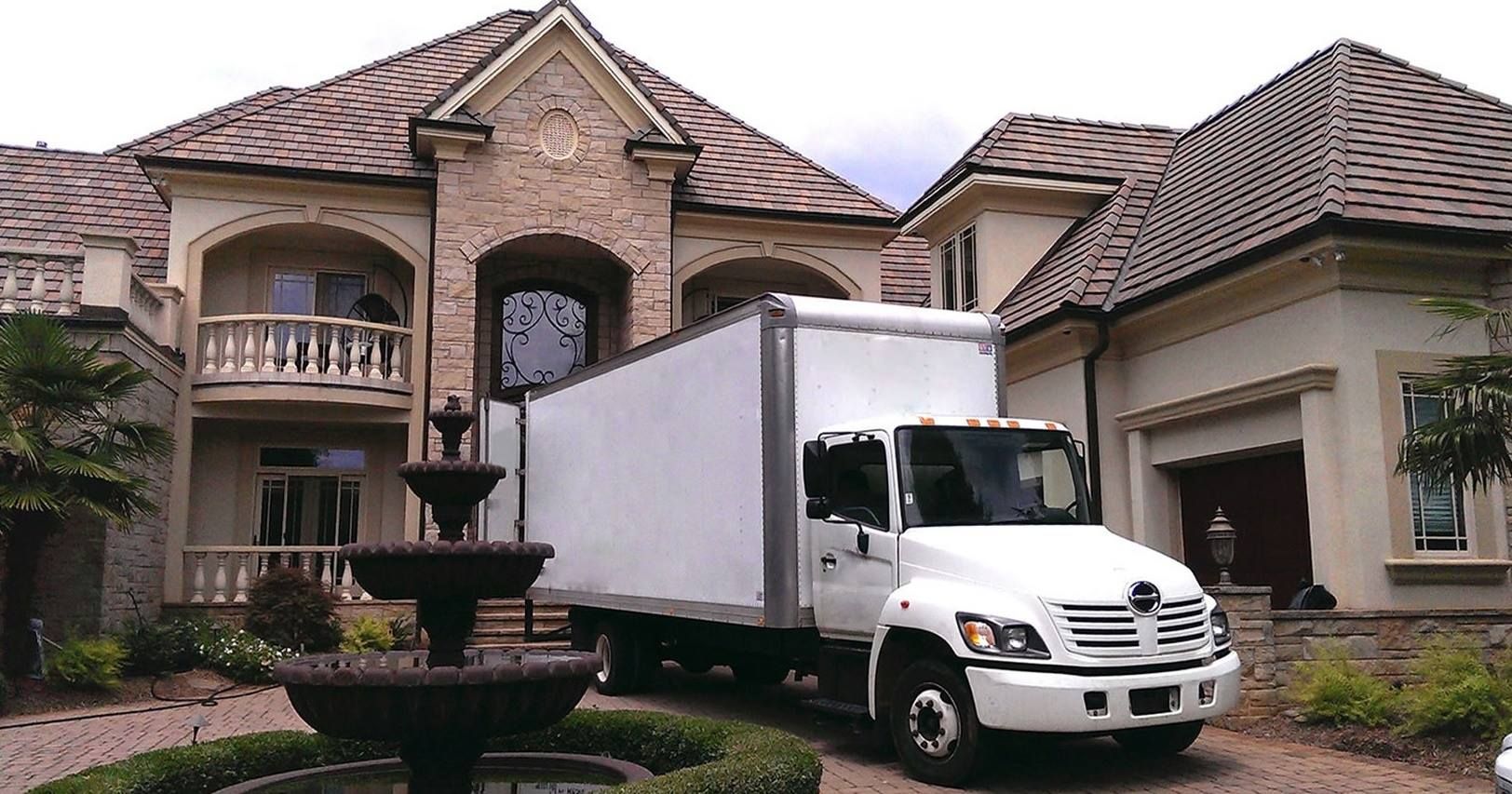 A white moving truck is parked in front of a large house