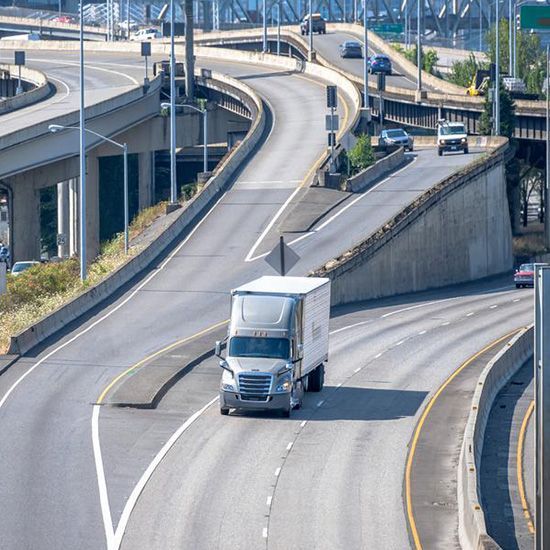 A semi truck is driving down a highway next to a bridge.
