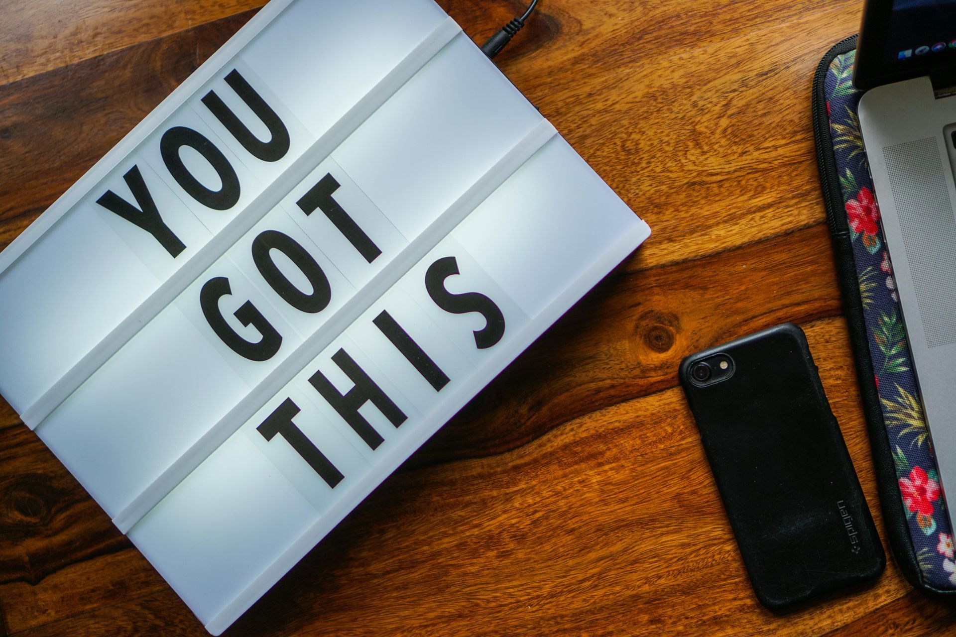 A sign that says `` you got this '' is on a wooden table next to a laptop and a cell phone. 28.4845° N, 81.2519° W