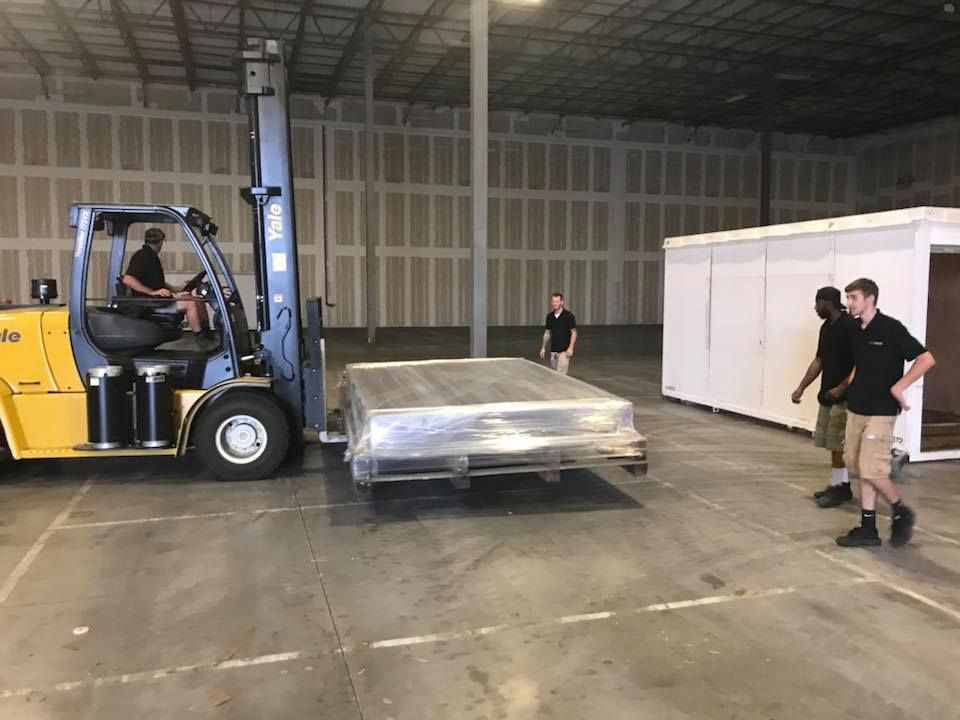 A forklift is moving a large piece of metal in a warehouse. 28.4845° N, 81.2519° W