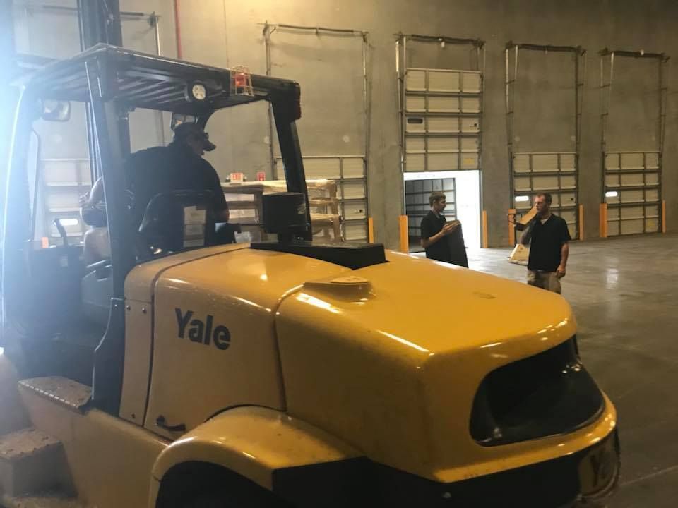 A man is driving a yellow forklift in a warehouse. 28.4845° N, 81.2519° W