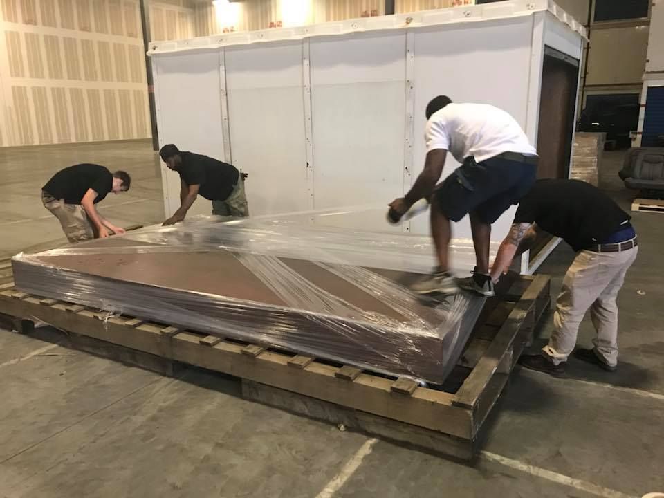 A group of men are wrapping a large piece of plastic on a wooden pallet. 28.4845° N, 81.2519° W