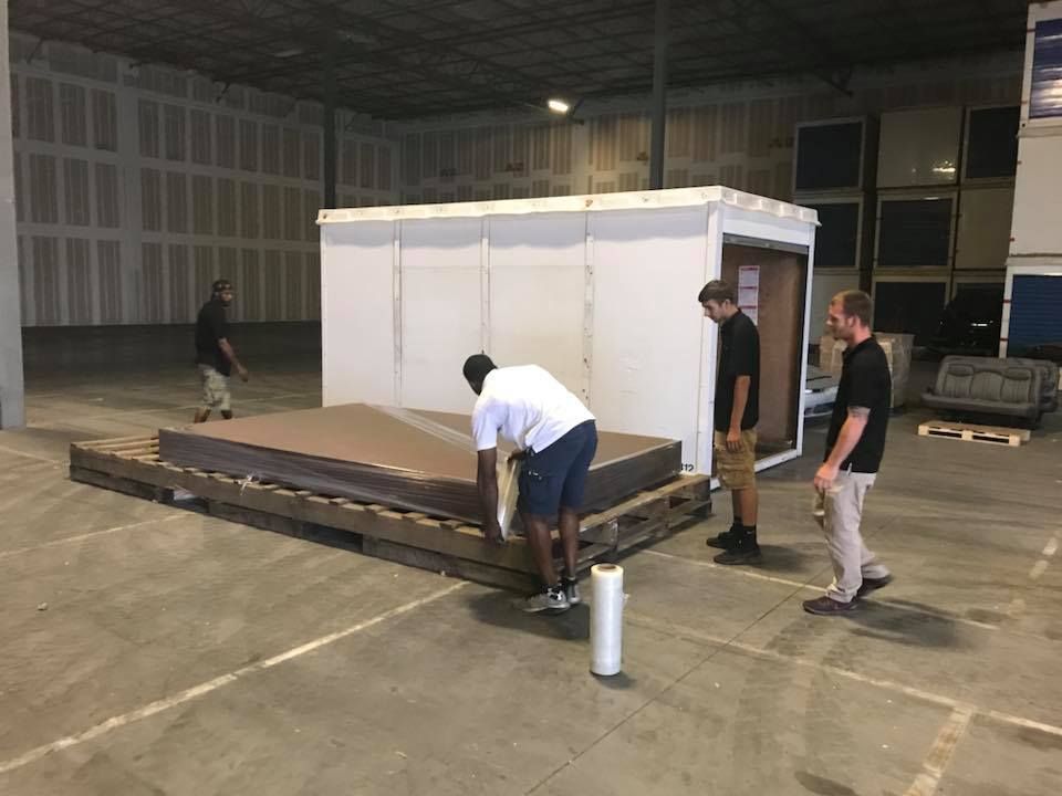 A group of men are standing around a large piece of wood in a warehouse. 28.4845° N, 81.2519° W