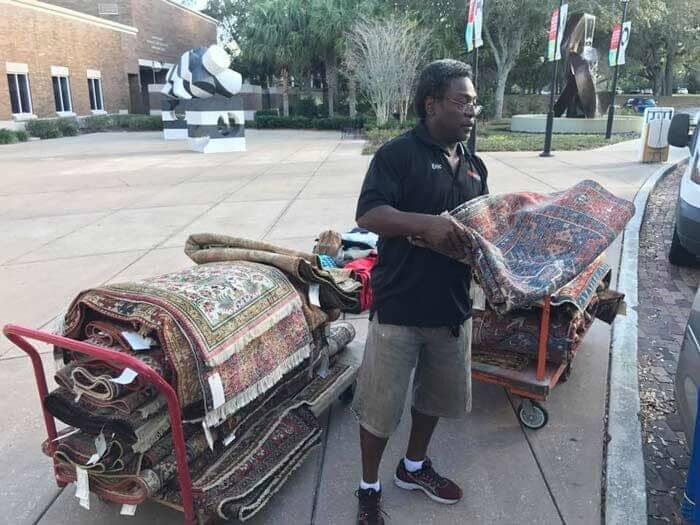 A man is standing next to a cart full of rugs.28.4845° N, 81.2519° W