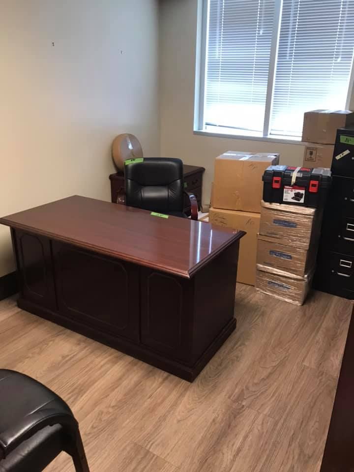A room with a desk , chair , boxes and a window. 28.4845° N, 81.2519° W