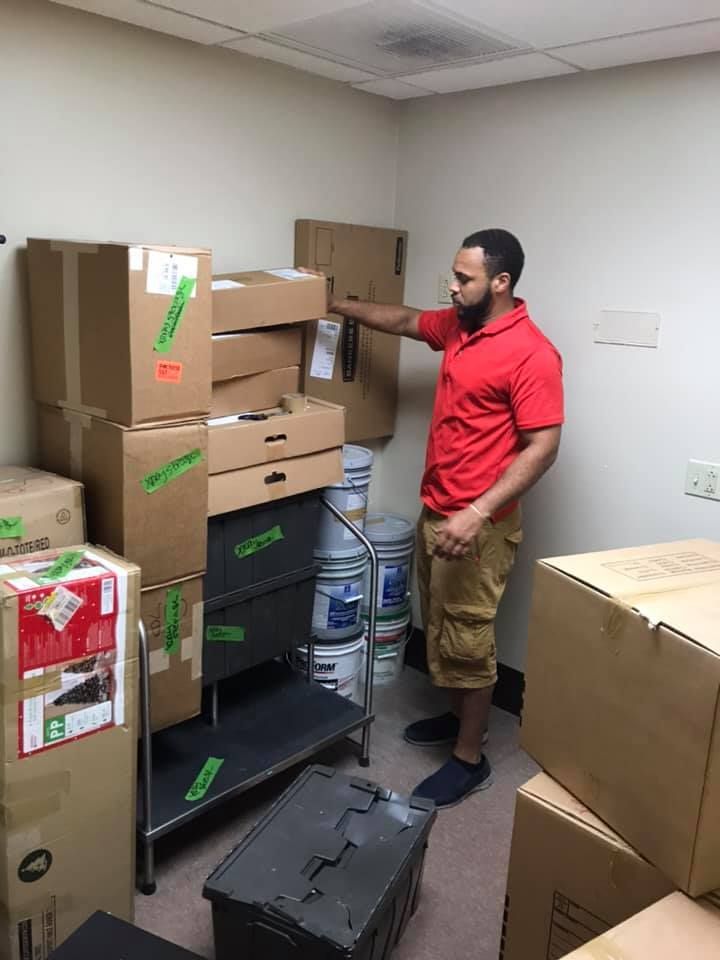 A man in a red shirt is standing in a room filled with boxes. 28.4845° N, 81.2519° W