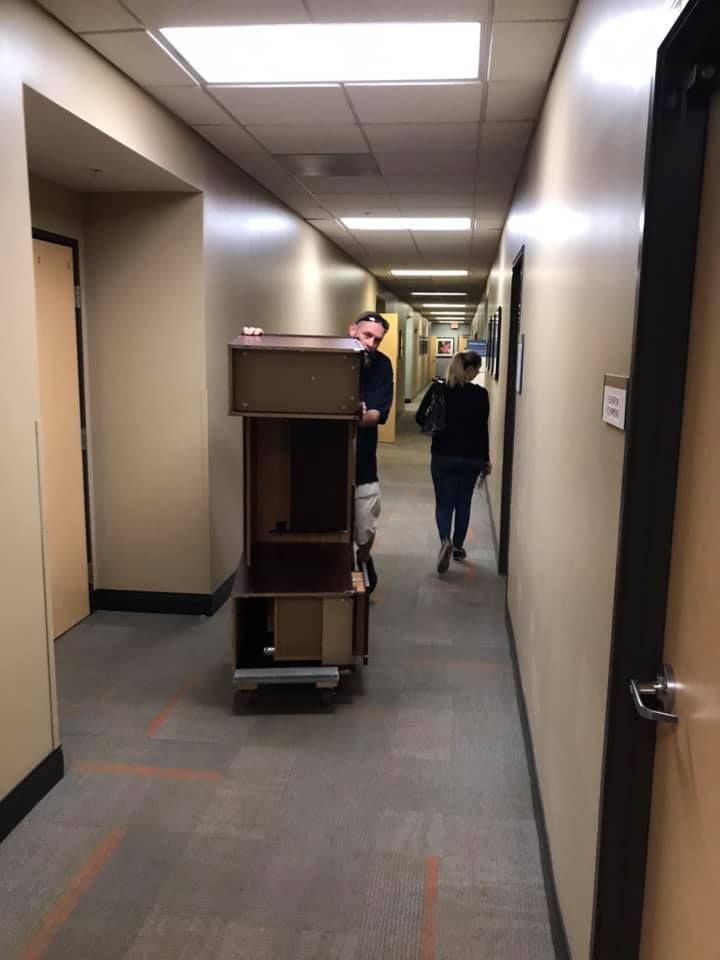 A man is pushing a cart with a dresser on it down a hallway. 28.4845° N, 81.2519° W