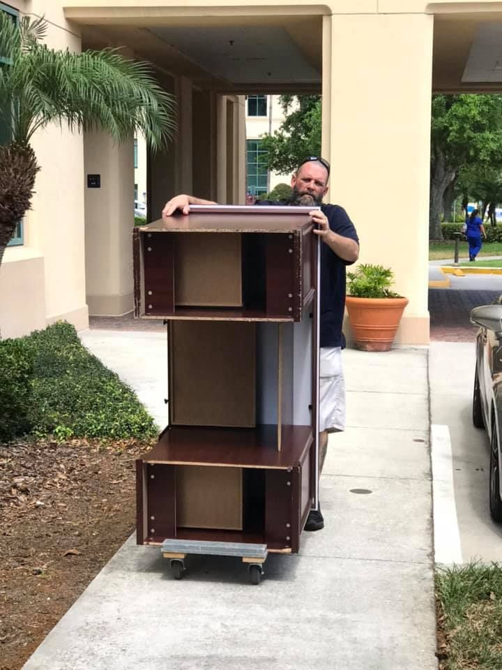 A man is carrying a stack of shelves on a dolly. 28.4845° N, 81.2519° W