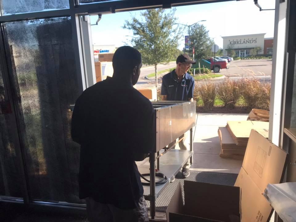 A man is standing in front of a window talking to another man. 28.4845° N, 81.2519° W