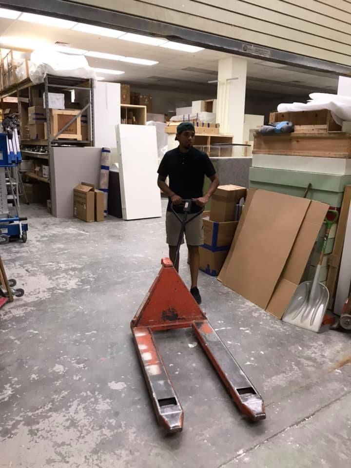 A man is standing next to a pallet truck in a warehouse. 28.4845° N, 81.2519° W