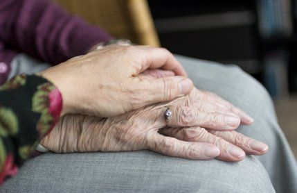 A woman is holding an older woman 's hand while sitting in a chair.