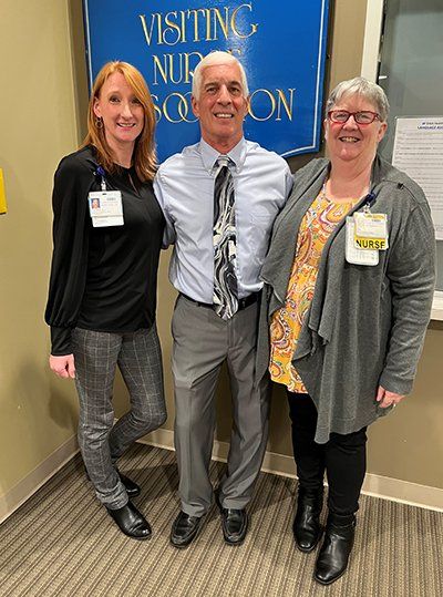 Three people are posing for a picture in front of a sign that says visiting nurses