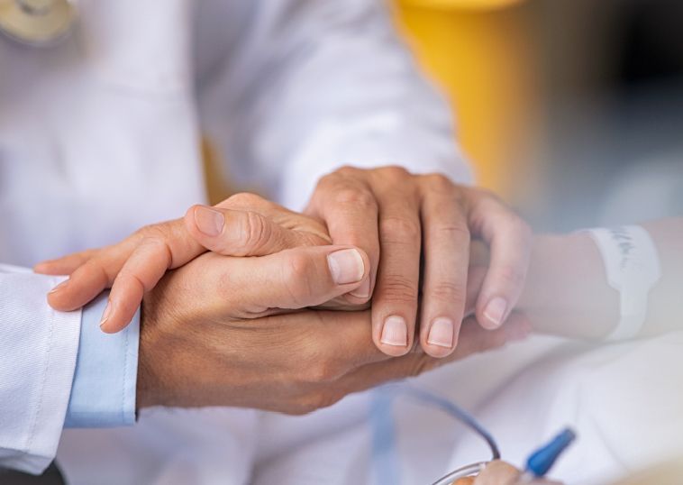 A doctor is holding a patient 's hand in a hospital room.