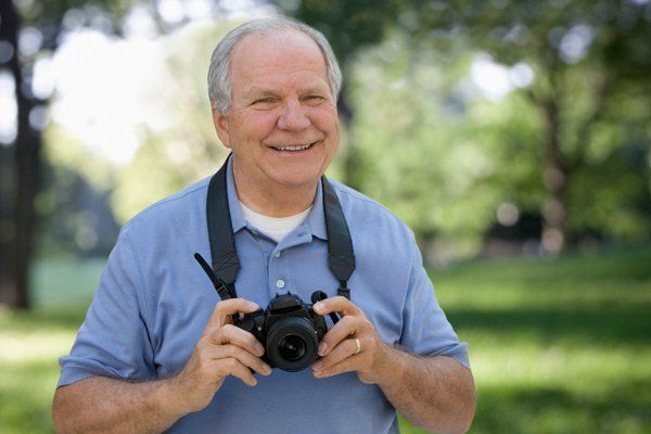 A man in a blue shirt is holding a camera and smiling