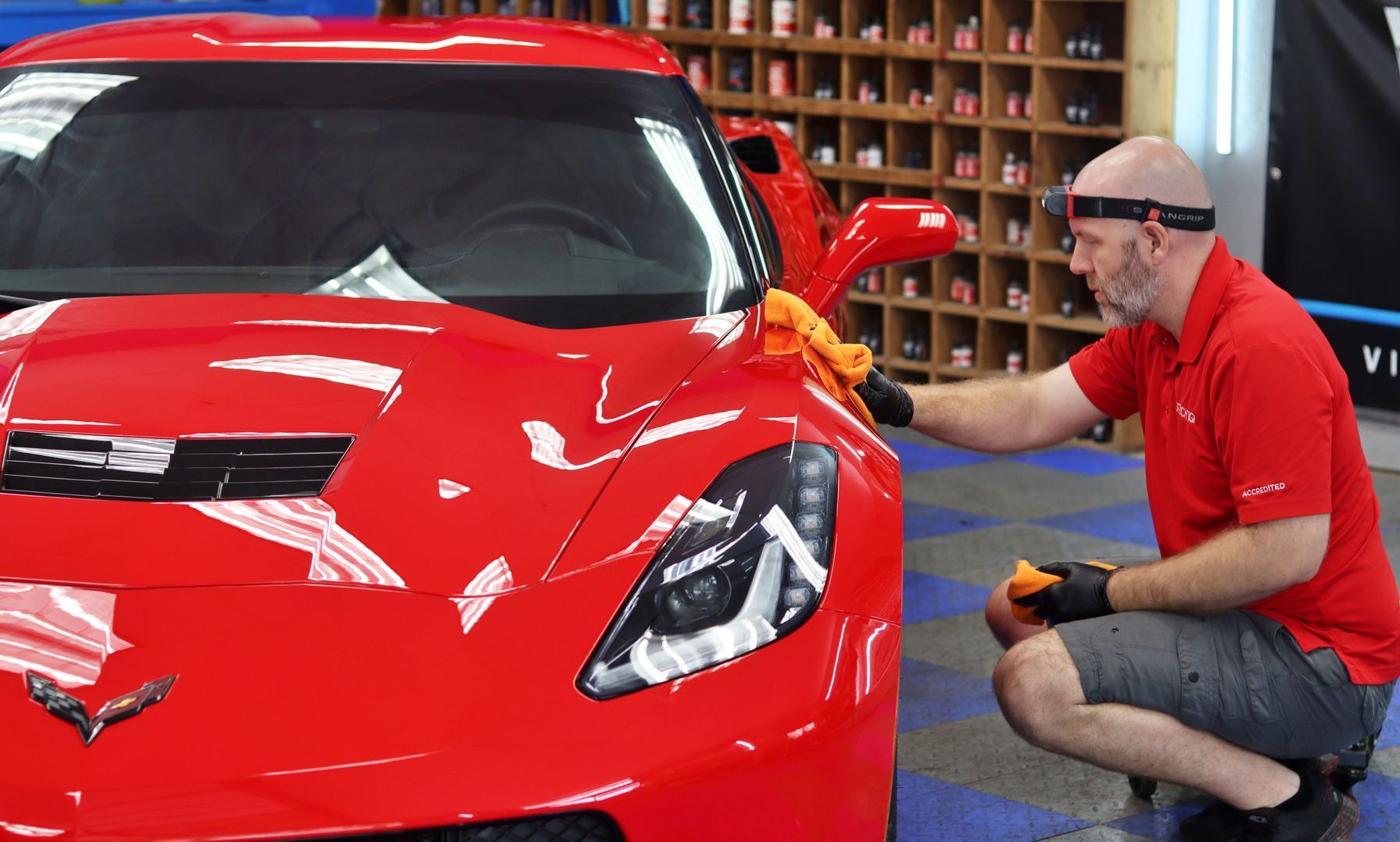 Detailing a red sports car in a garage, with a technician polishing the front fender with a cloth