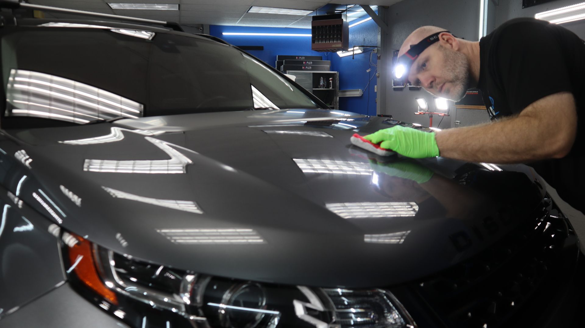 A man is polishing the hood of a car in a garage.