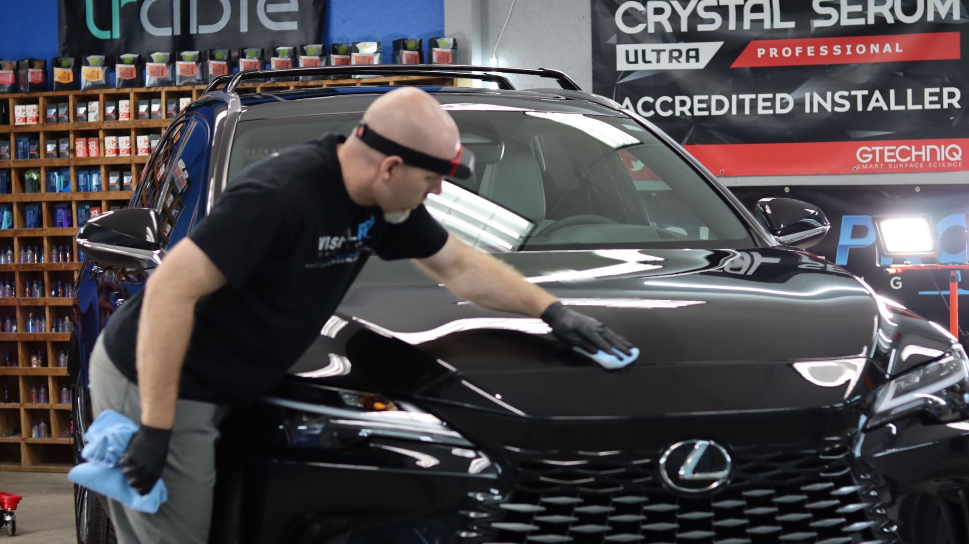A man is polishing the hood of a black lexus suv.