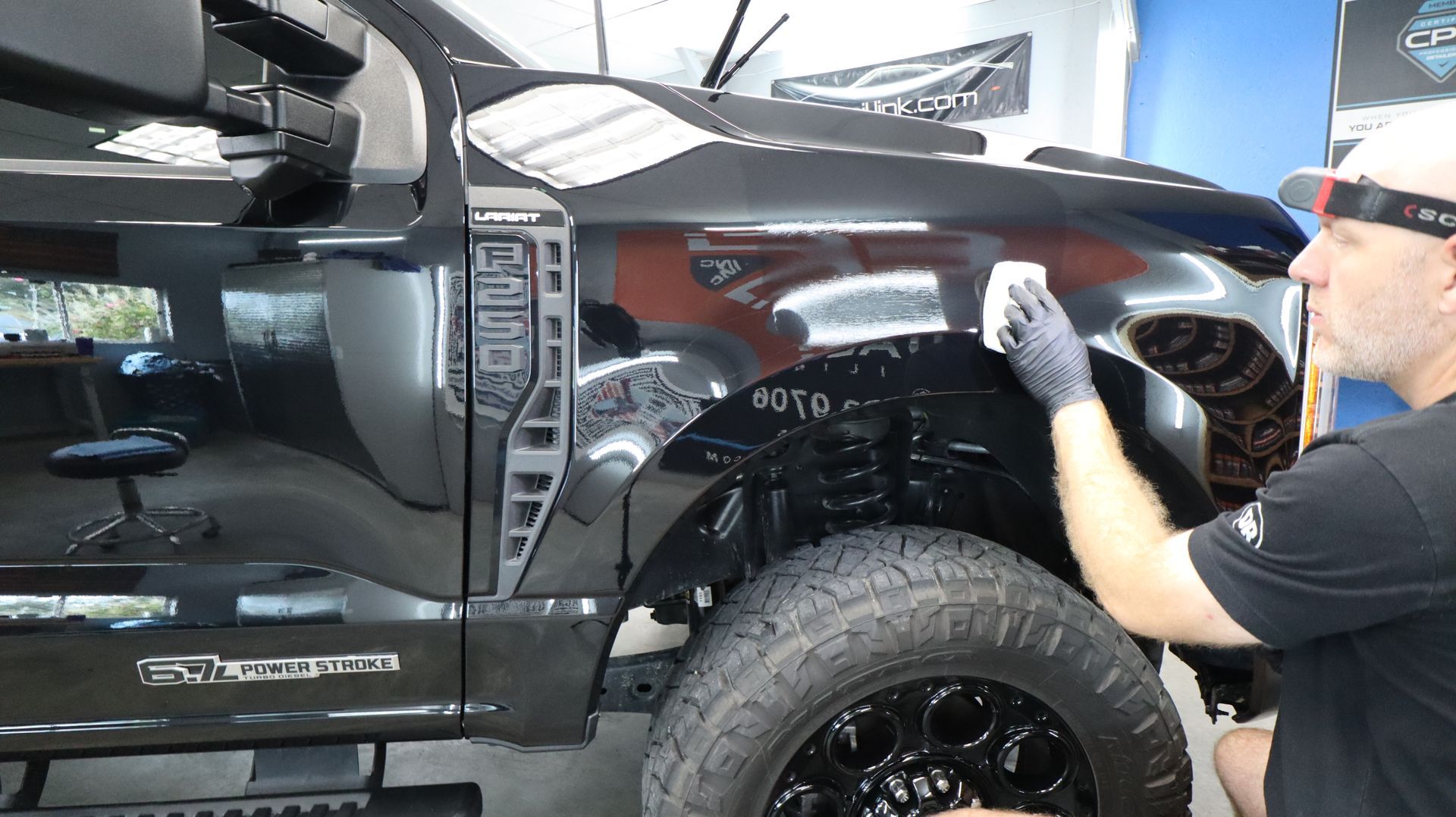 Mechanic polishing a black truck’s front fender in a workshop