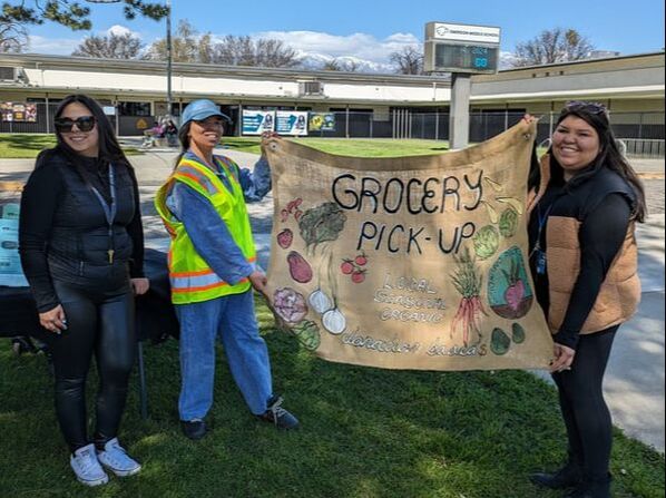 Three people stand outside holding a burlap sign that reads