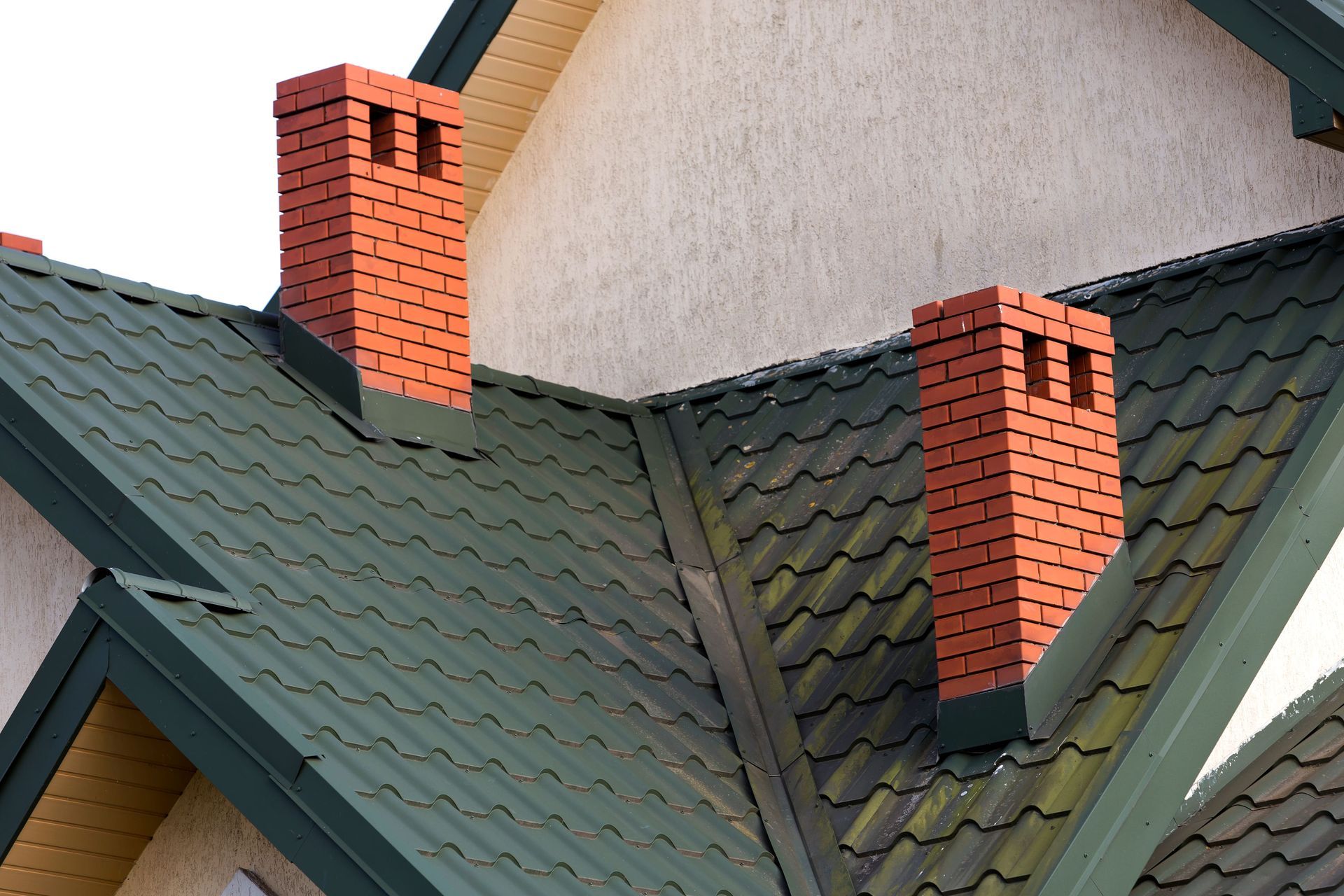Two red brick chimneys on a dark green shingled roof with light stucco walls