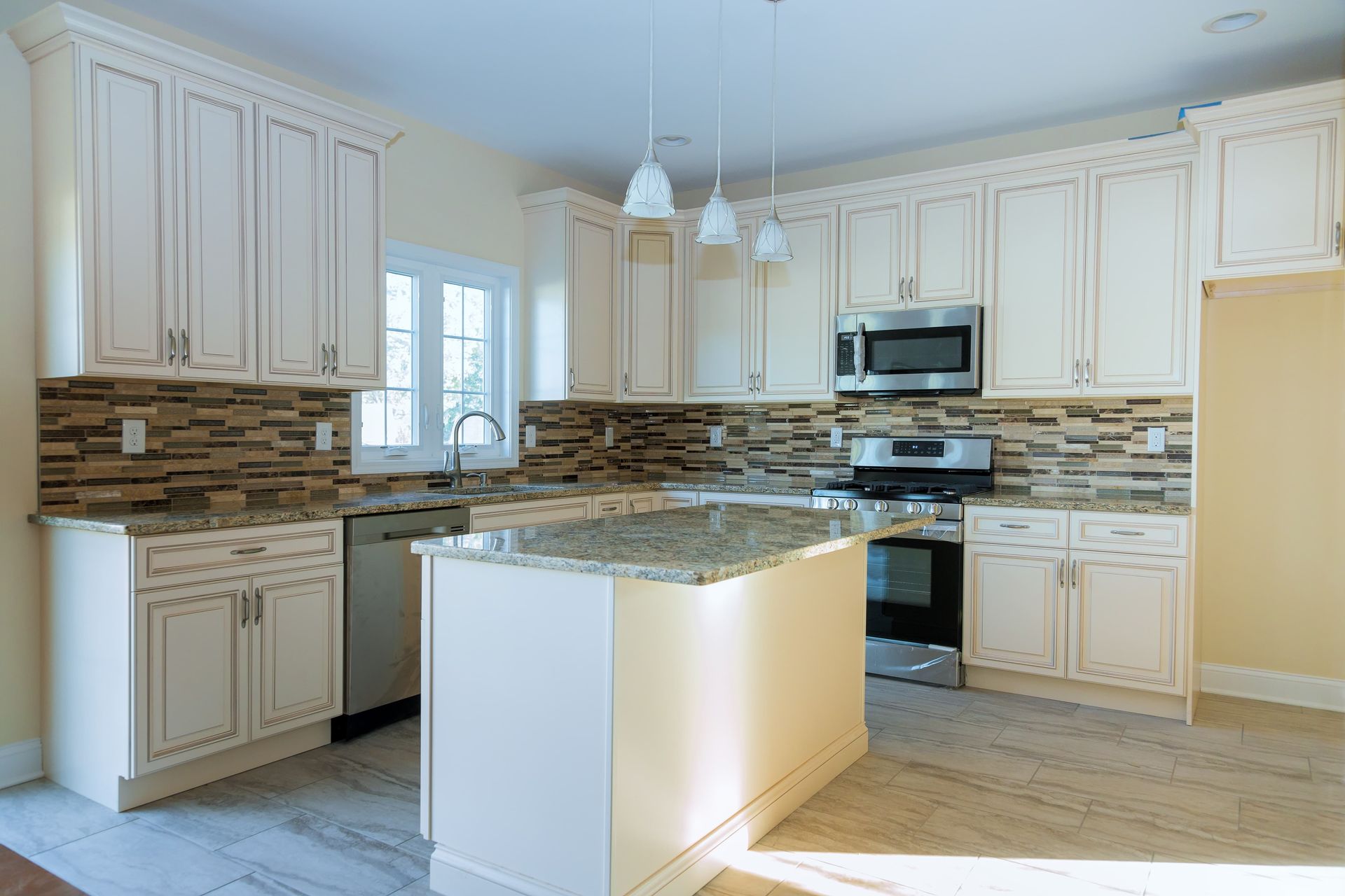 Bright modern kitchen with cream cabinets, granite island, and stainless steel appliances.