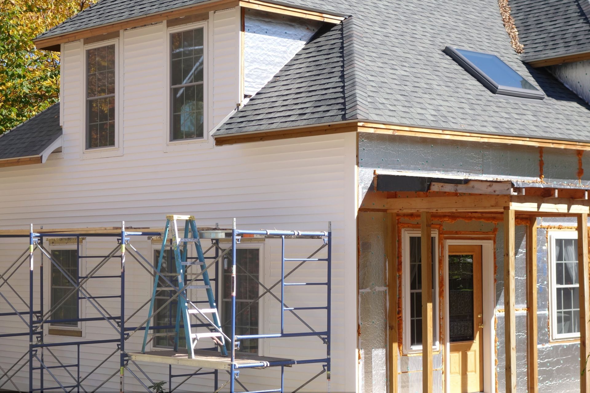 House exterior under construction with scaffolding and ladders by a gray-shingled roof