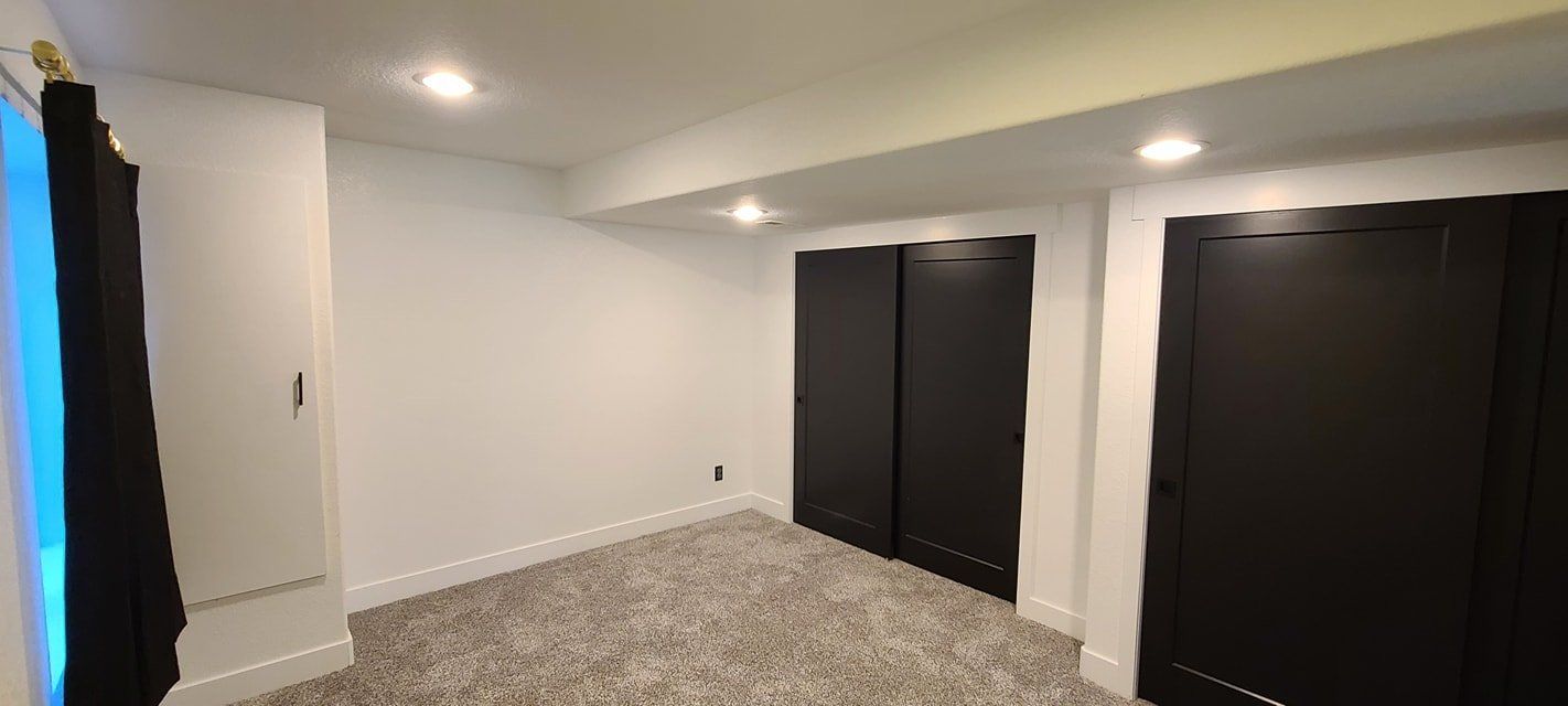 An empty room with a carpeted floor and black doors.