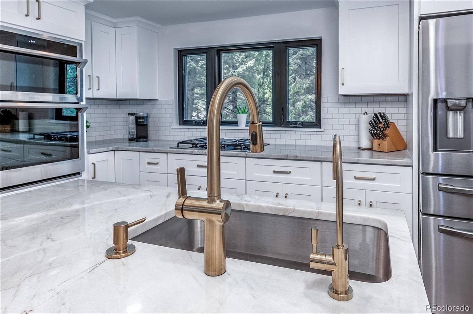 A kitchen with white cabinets , stainless steel appliances , a sink and a refrigerator.